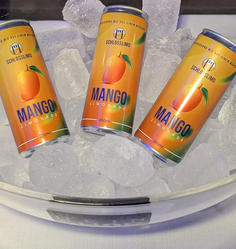 Drei Dosen Schlosslimo Mango liegen auf Eiswürfeln.